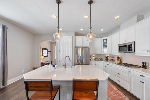 kitchen featuring stainless steel appliances, arched walkways, light countertops, and white cabinetry