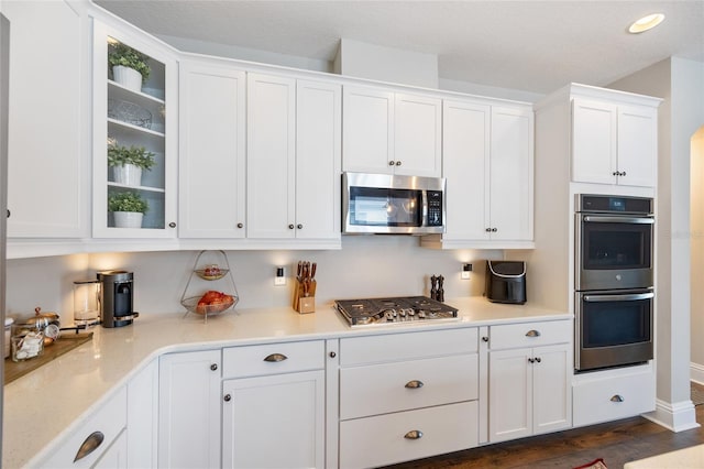 kitchen with dark wood finished floors, recessed lighting, appliances with stainless steel finishes, glass insert cabinets, and white cabinetry