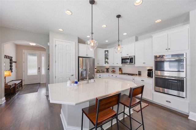kitchen with arched walkways, appliances with stainless steel finishes, white cabinets, and glass insert cabinets