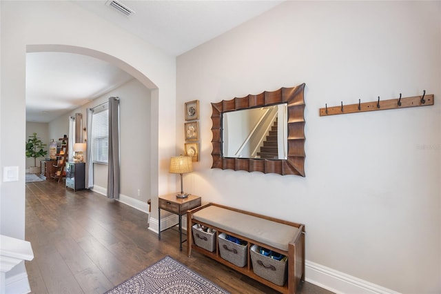 corridor with arched walkways, baseboards, wood finished floors, and visible vents