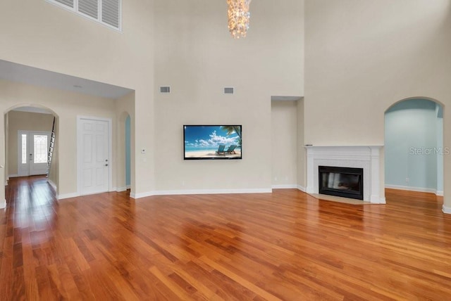 unfurnished living room featuring arched walkways, light wood-type flooring, a fireplace with flush hearth, and visible vents