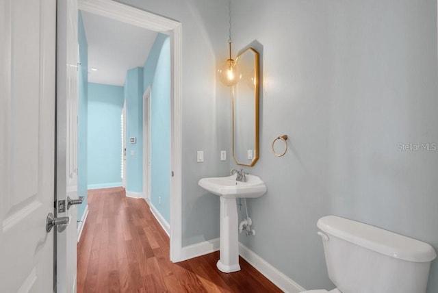 half bathroom with wood finished floors, toilet, and baseboards