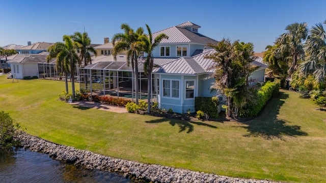 rear view of property featuring a water view, a lawn, a standing seam roof, glass enclosure, and metal roof