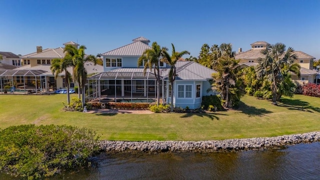 rear view of property featuring a water view, a lawn, a standing seam roof, metal roof, and a lanai