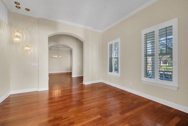 spare room featuring baseboards, arched walkways, ornamental molding, wood finished floors, and an inviting chandelier