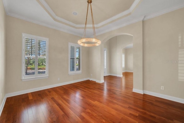 empty room with arched walkways, baseboards, ornamental molding, wood-type flooring, and a raised ceiling