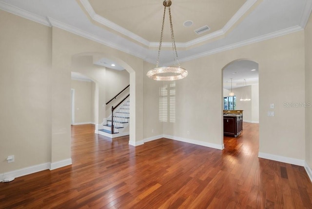 empty room featuring a tray ceiling, dark wood-style flooring, visible vents, and baseboards