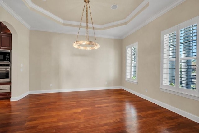 interior space with arched walkways, crown molding, a raised ceiling, wood finished floors, and baseboards