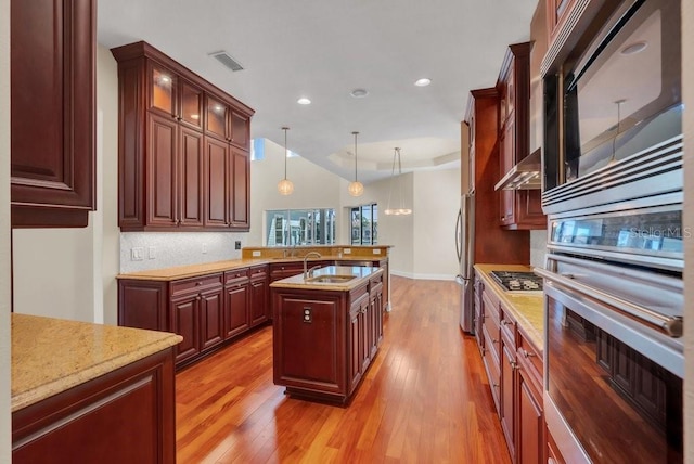 kitchen featuring light stone counters, pendant lighting, light wood finished floors, stainless steel appliances, and a peninsula