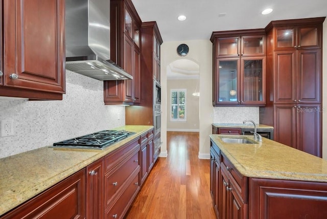 kitchen with reddish brown cabinets, appliances with stainless steel finishes, a sink, light wood-type flooring, and wall chimney exhaust hood