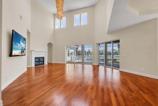 unfurnished living room featuring wood-type flooring, visible vents, baseboards, and a glass covered fireplace