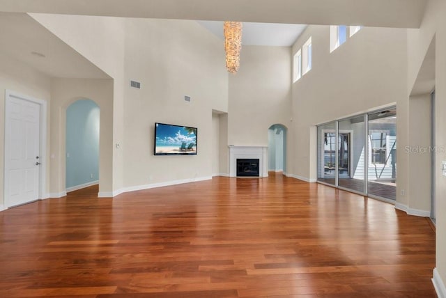 unfurnished living room featuring arched walkways, a fireplace, visible vents, wood finished floors, and baseboards