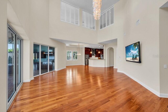 unfurnished living room with light wood-type flooring, baseboards, arched walkways, and a notable chandelier