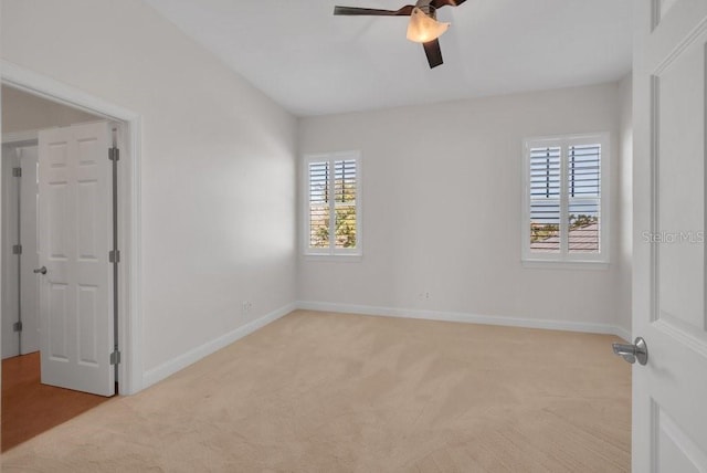 empty room featuring a ceiling fan, light colored carpet, and baseboards