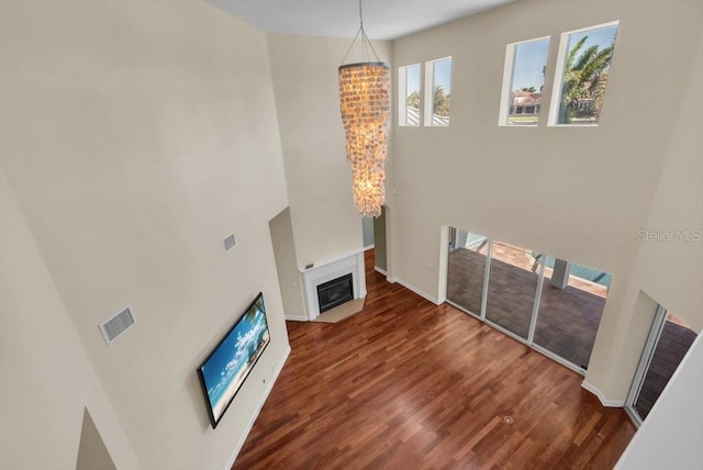 unfurnished living room with visible vents, a high ceiling, a fireplace with flush hearth, wood finished floors, and a chandelier