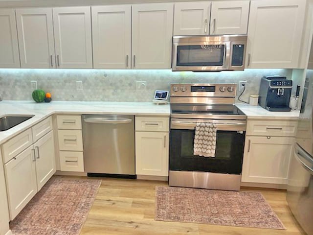 kitchen featuring light wood-type flooring, a sink, backsplash, appliances with stainless steel finishes, and light countertops