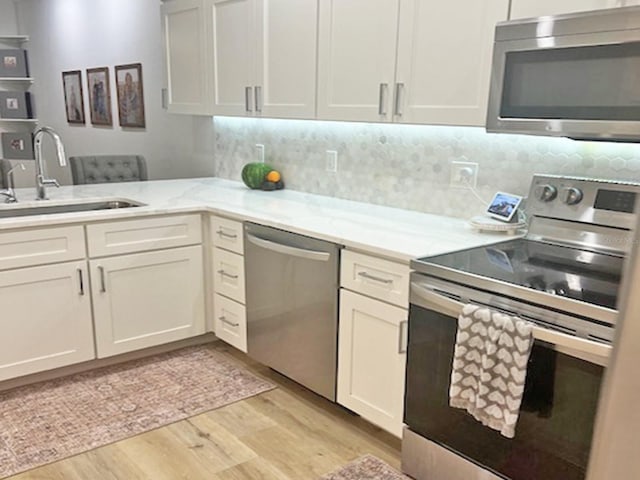 kitchen featuring tasteful backsplash, appliances with stainless steel finishes, light wood-style floors, and a sink