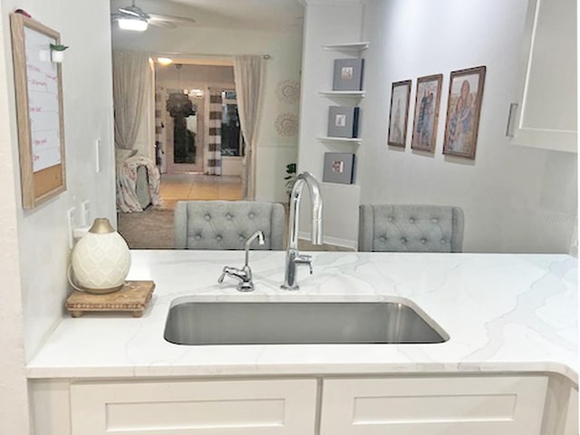 interior space featuring a sink, light stone counters, a ceiling fan, and white cabinetry