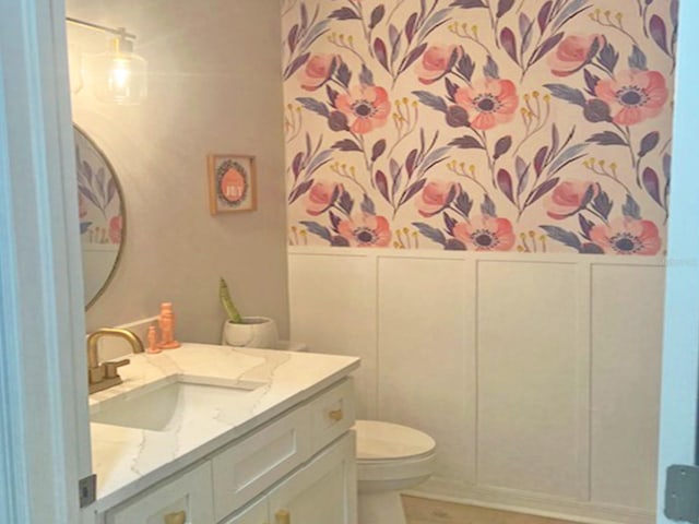 bathroom featuring wainscoting, a decorative wall, toilet, and vanity