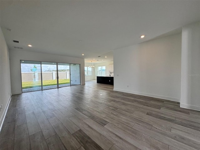 unfurnished living room with visible vents, baseboards, dark wood-style flooring, an inviting chandelier, and recessed lighting