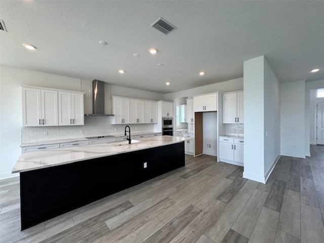 kitchen with a spacious island, black electric stovetop, light wood-style floors, and wall chimney exhaust hood