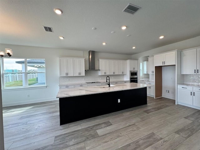 kitchen featuring wall chimney exhaust hood, visible vents, white cabinets, and a large island with sink