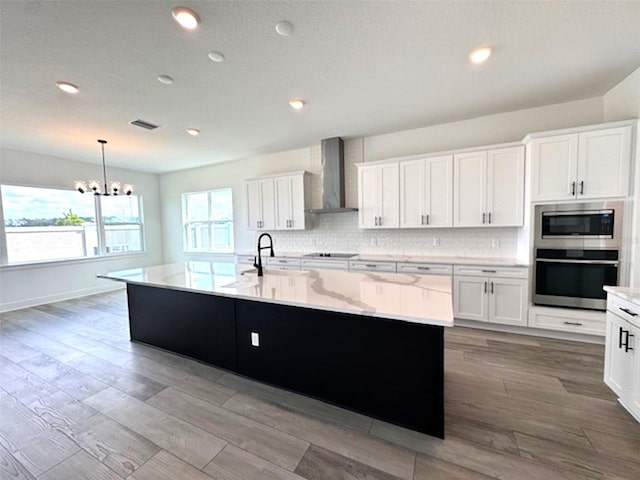 kitchen featuring appliances with stainless steel finishes, white cabinetry, wall chimney range hood, and tasteful backsplash