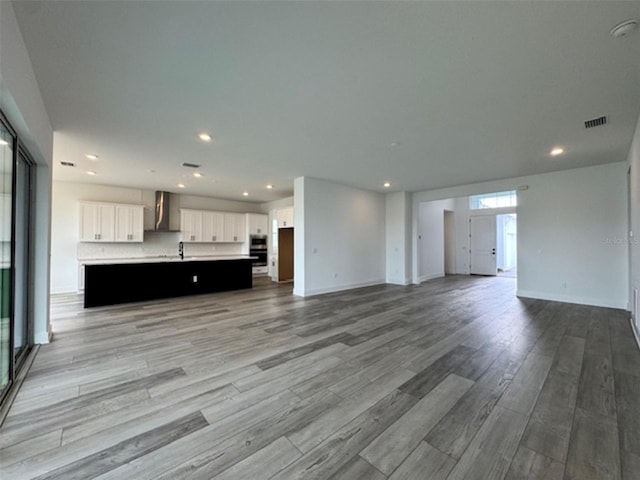 unfurnished living room featuring light wood finished floors, recessed lighting, visible vents, a sink, and baseboards