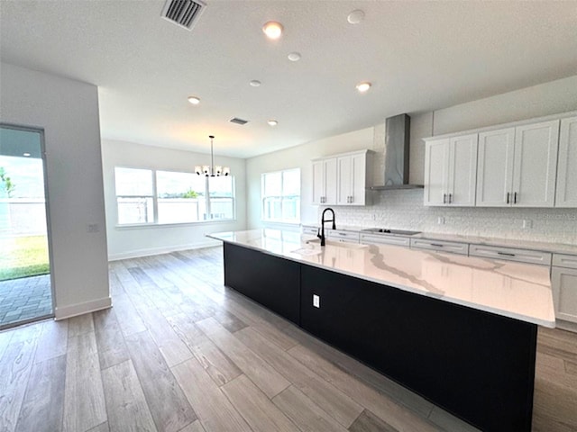 kitchen featuring visible vents, decorative backsplash, light wood-type flooring, a large island with sink, and wall chimney exhaust hood