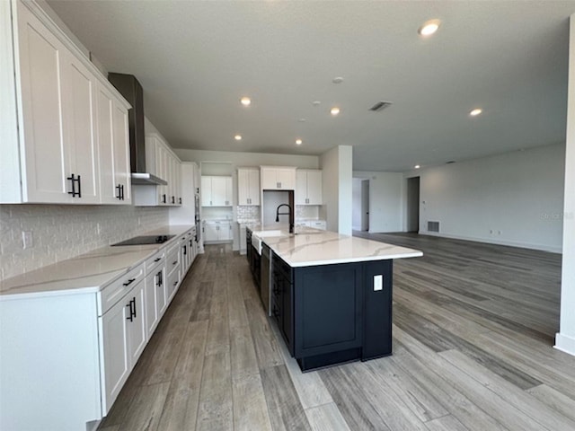 kitchen with light wood-type flooring, wall chimney exhaust hood, white cabinets, and a sink