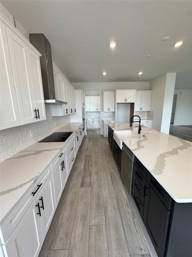 kitchen featuring black electric stovetop, light wood-style floors, white cabinets, a sink, and wall chimney exhaust hood