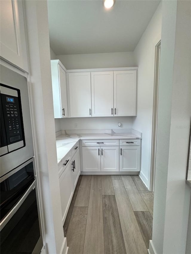 kitchen featuring light stone counters, baseboards, white cabinets, appliances with stainless steel finishes, and light wood finished floors