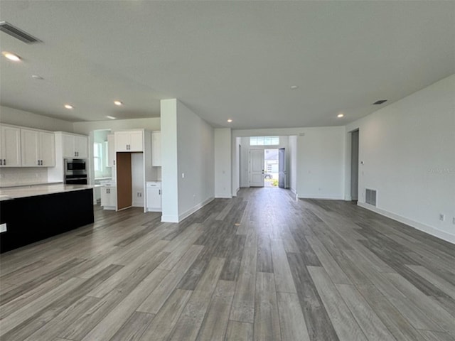 unfurnished living room featuring baseboards, light wood-type flooring, visible vents, and recessed lighting