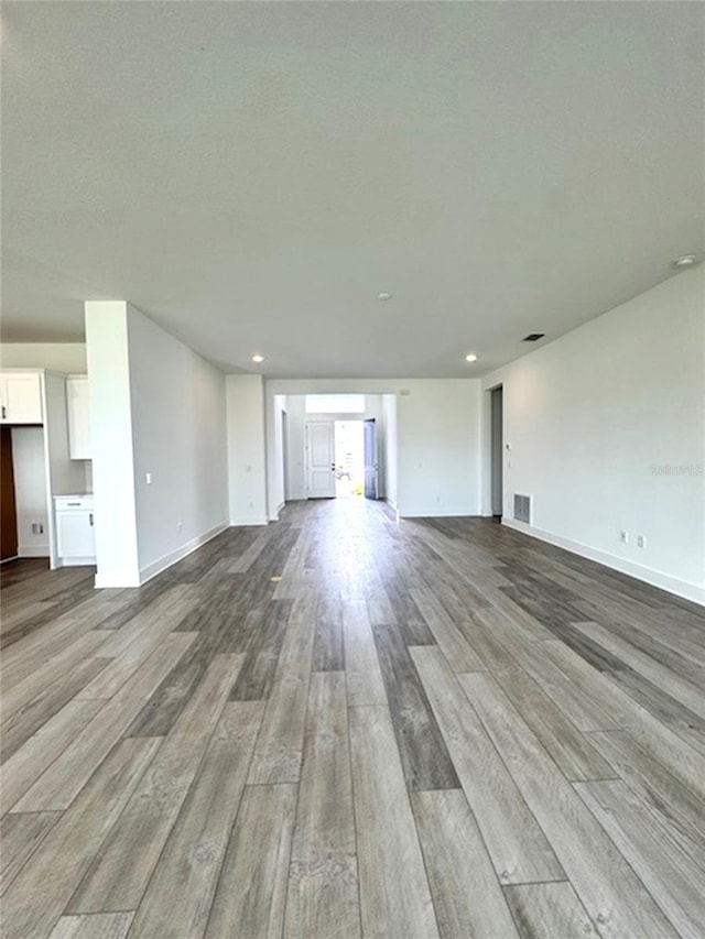 unfurnished living room featuring baseboards, a textured ceiling, visible vents, and wood finished floors