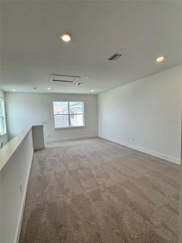 unfurnished room featuring light carpet, a textured ceiling, attic access, and baseboards