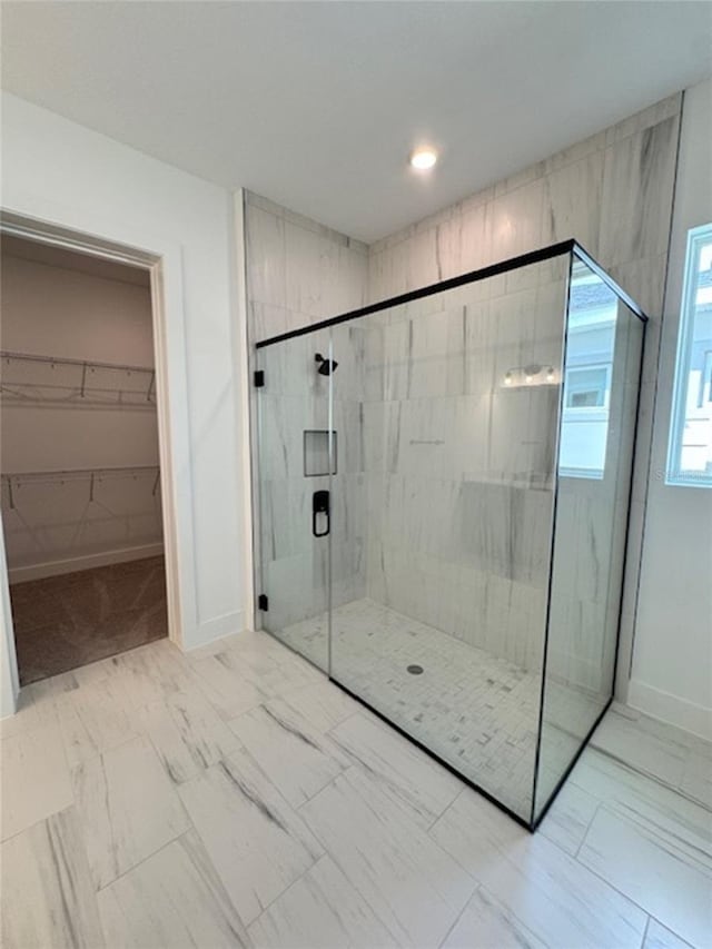 bathroom featuring marble finish floor, a marble finish shower, baseboards, and a walk in closet