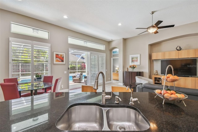 kitchen featuring light brown cabinets, dark stone counters, recessed lighting, ceiling fan, and a sink