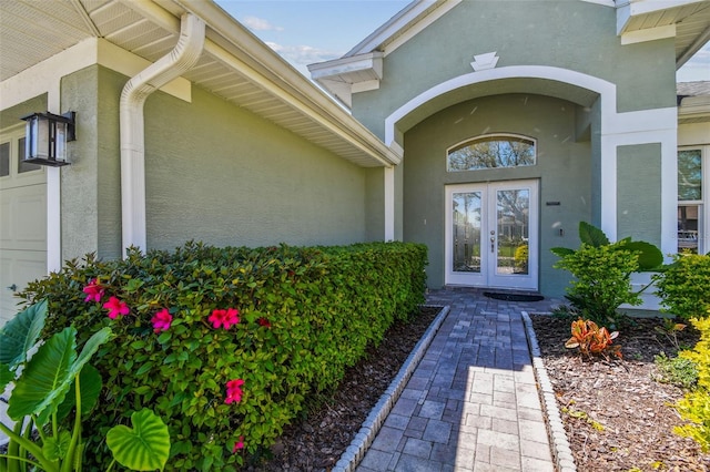 view of exterior entry with an attached garage, french doors, and stucco siding