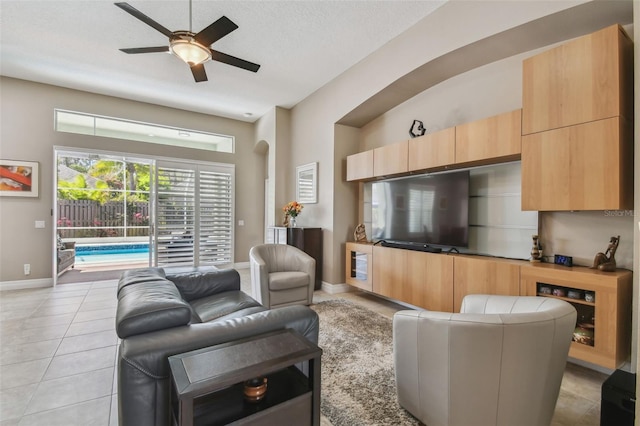 living room with light tile patterned flooring, a textured ceiling, baseboards, and a ceiling fan