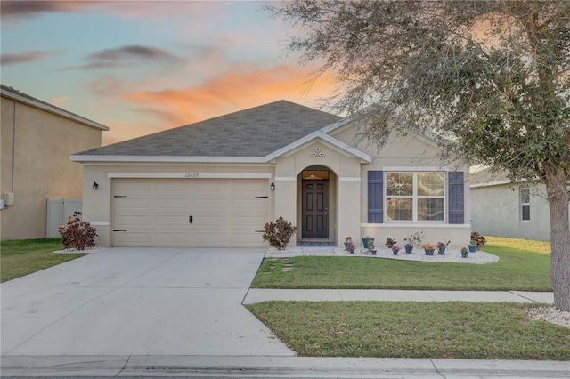 single story home featuring roof with shingles, stucco siding, concrete driveway, a garage, and a front lawn