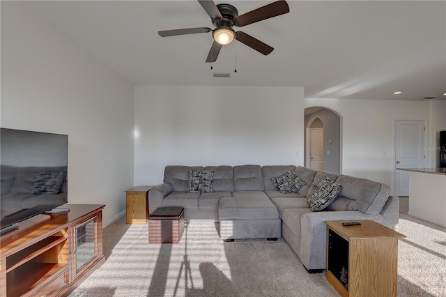 living room featuring arched walkways, a ceiling fan, visible vents, and light colored carpet