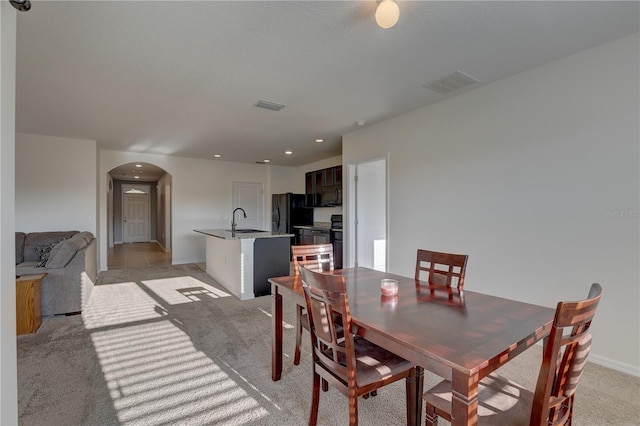 dining space featuring arched walkways, baseboards, visible vents, and light colored carpet