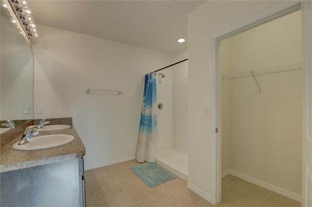 bathroom with a spacious closet, tiled shower, tile patterned flooring, and a sink