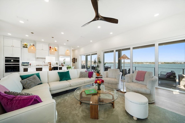 living area with recessed lighting, a water view, ceiling fan, and wood finished floors