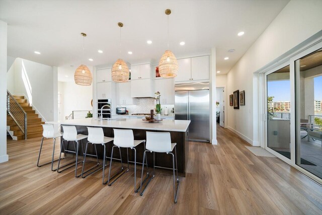 kitchen with stainless steel appliances, tasteful backsplash, light countertops, white cabinetry, and a large island with sink