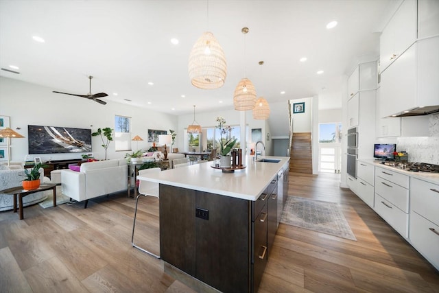 kitchen featuring light countertops, appliances with stainless steel finishes, open floor plan, a sink, and wood finished floors