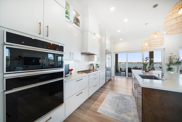 kitchen with light countertops, dobule oven black, light wood-style flooring, backsplash, and a sink