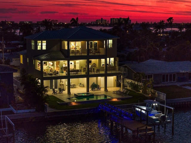 back of property at dusk featuring boat lift, a patio area, a balcony, an in ground hot tub, and an outdoor pool