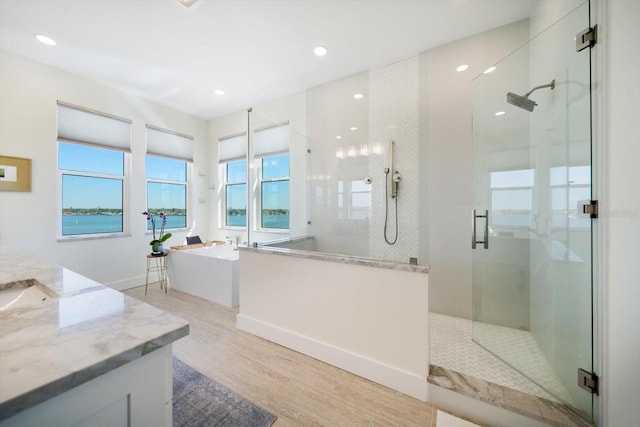 full bath featuring a stall shower, vanity, a freestanding bath, and wood finished floors