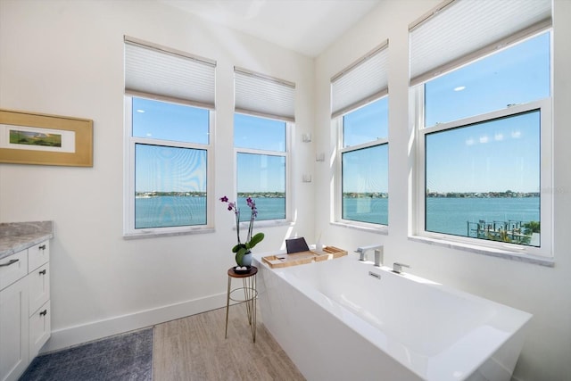 full bath featuring a soaking tub, vanity, baseboards, and wood finished floors